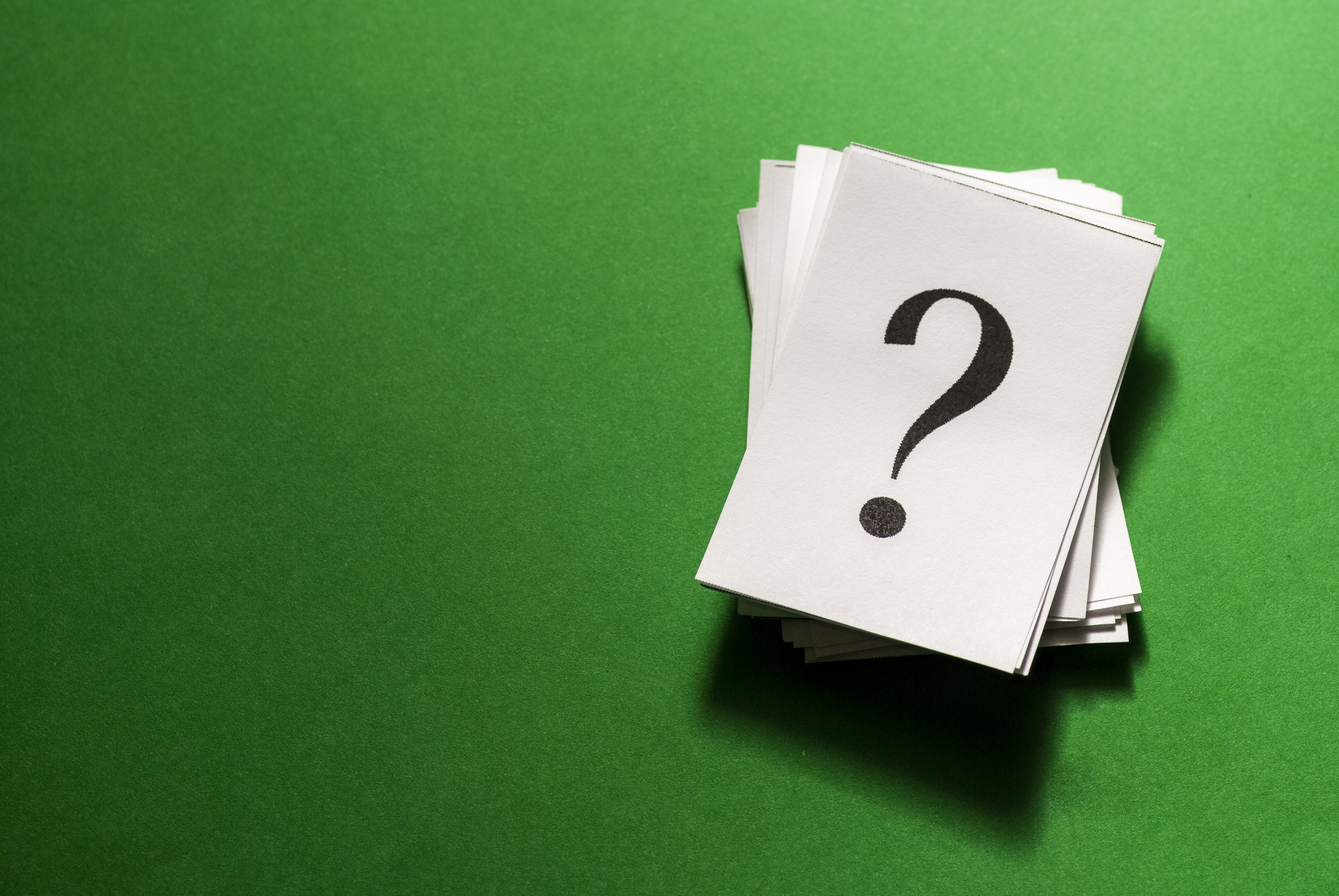 Pile of stacked question marks printed on white paper viewed from overhead on a green background with copy space